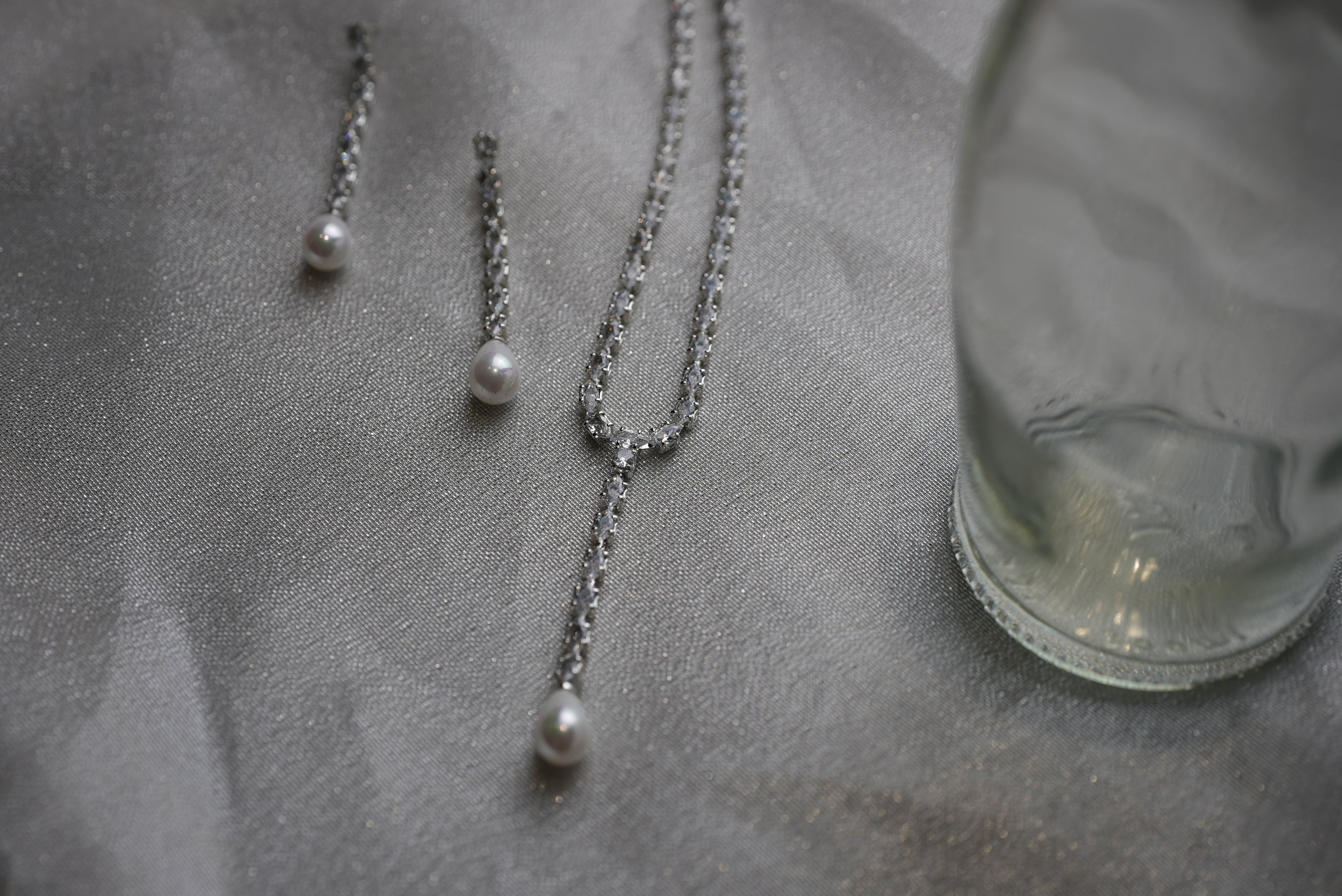 Pearl necklace and earrings on a textured surface with a glass object.