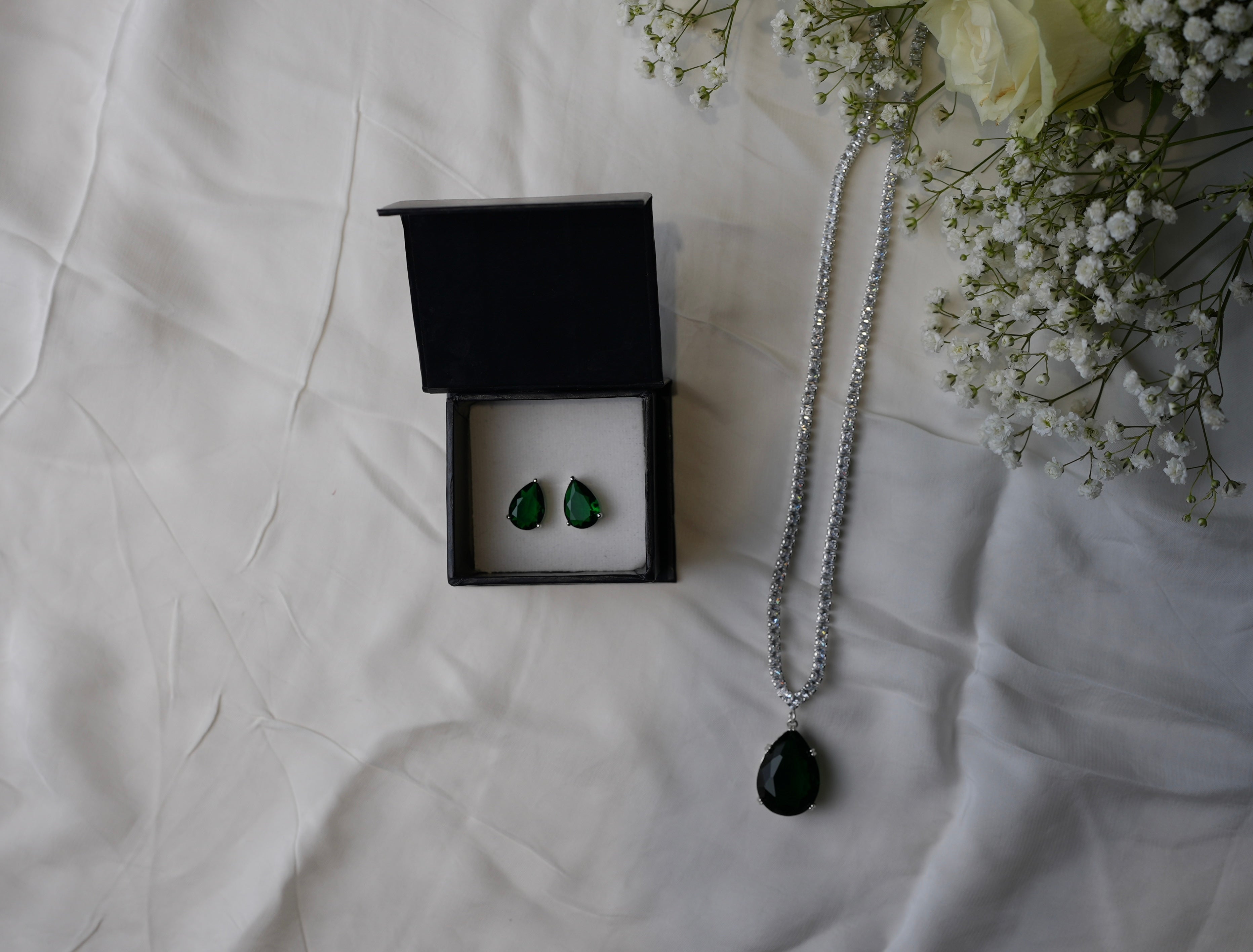Jewelry set with earrings and necklace on a textured surface with flowers.