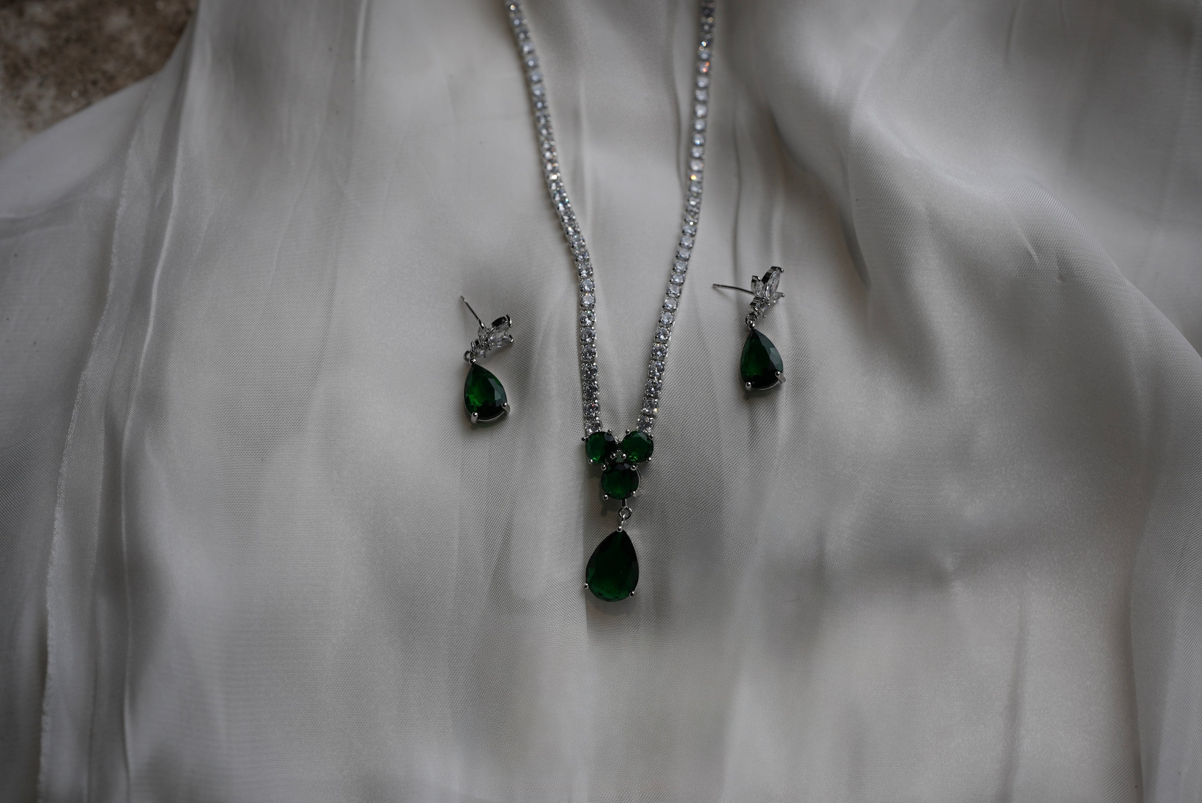 Jewelry set with green teardrop pendants on a white fabric background