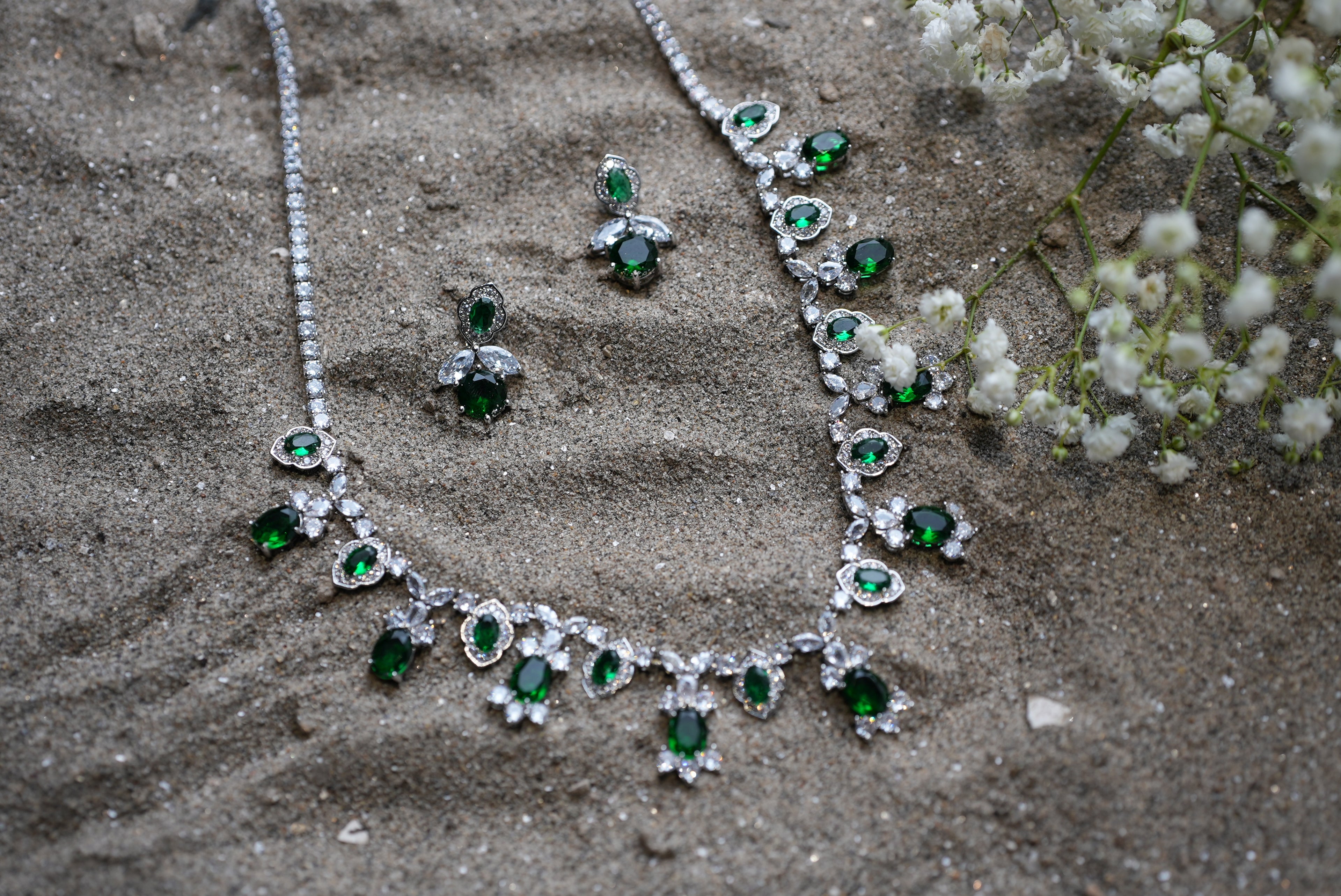 Jewelry set with necklace and earrings on a textured surface with small white flowers.