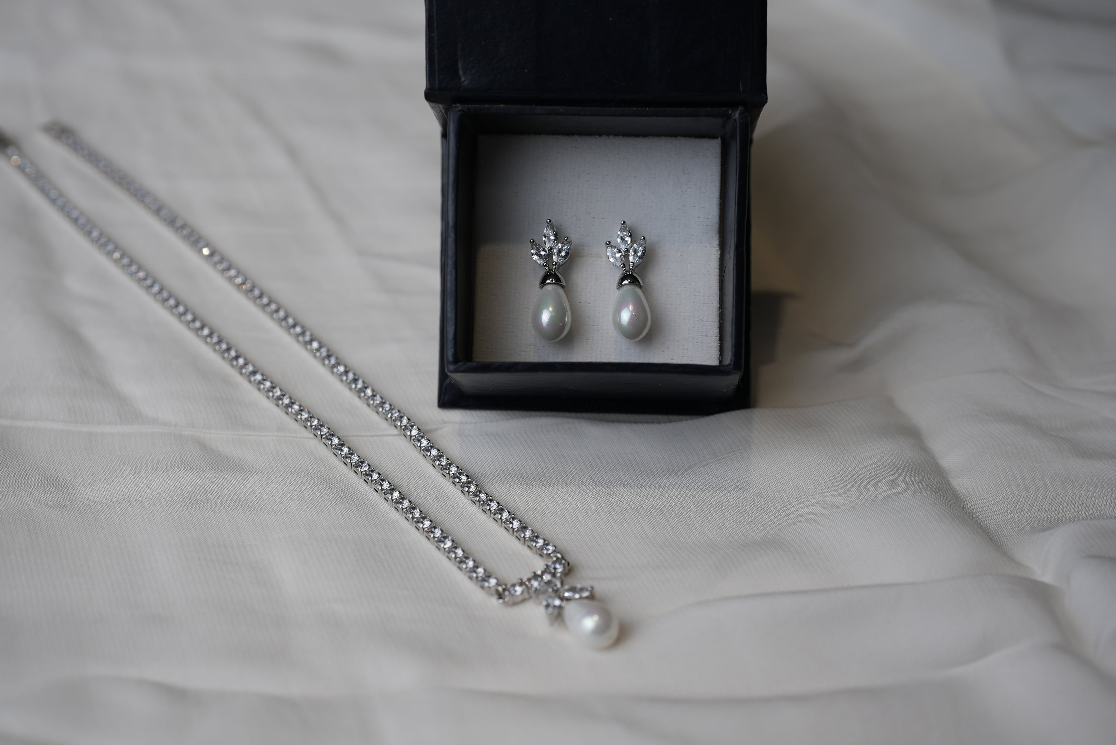 Pearl necklace and earrings in a black box on a white fabric background