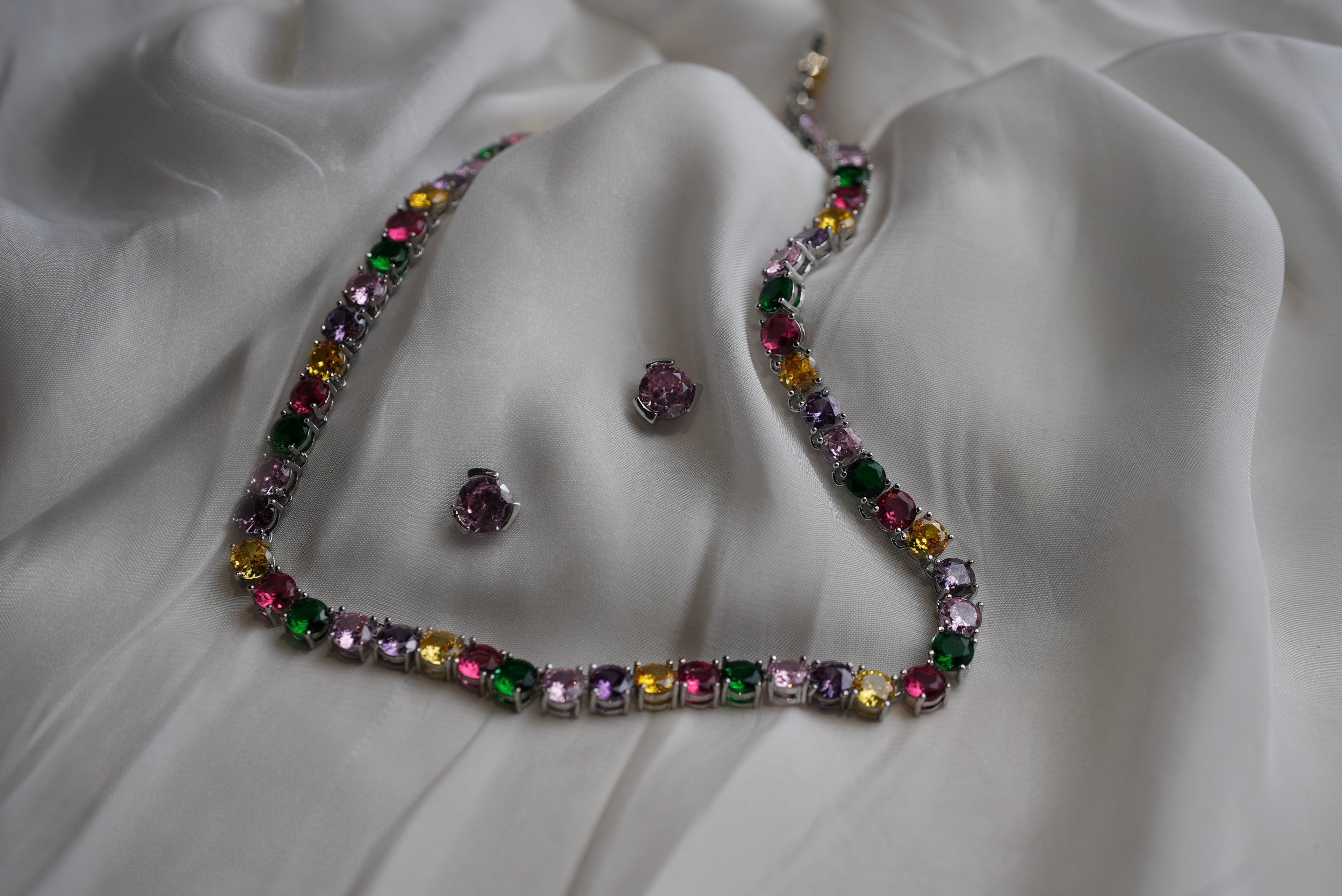 Multicolored gemstone necklace and earrings on a white fabric background