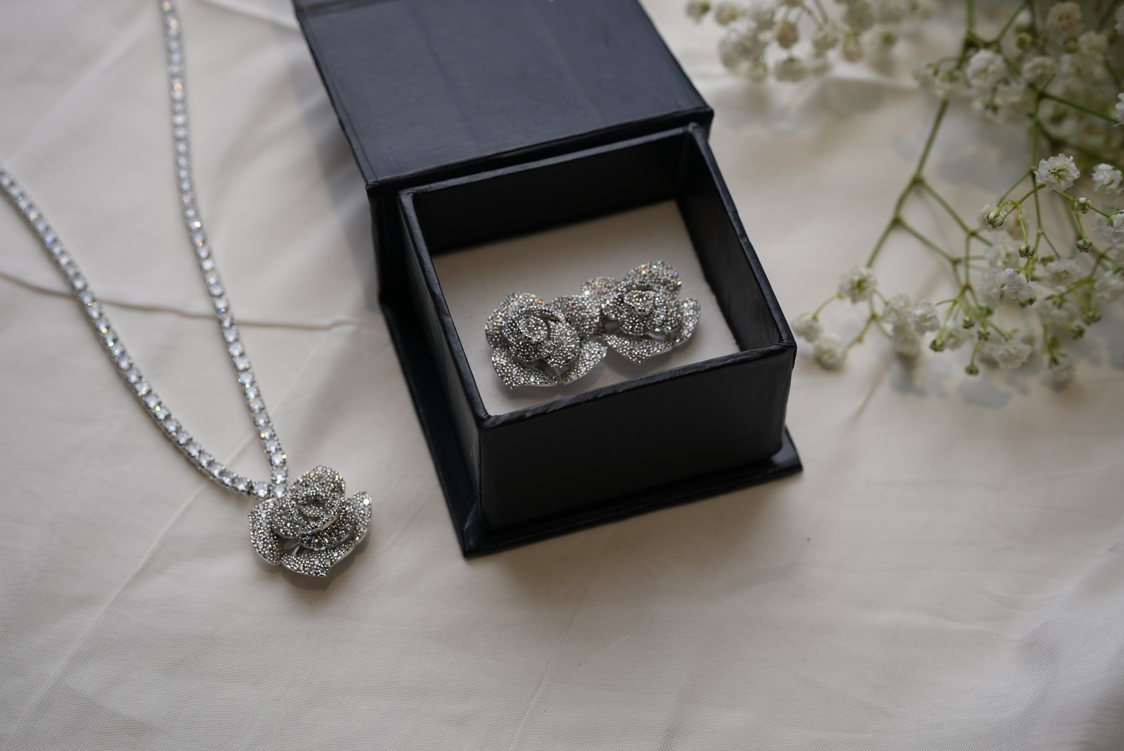 Silver rose-shaped jewelry set with necklace and earrings on a light background