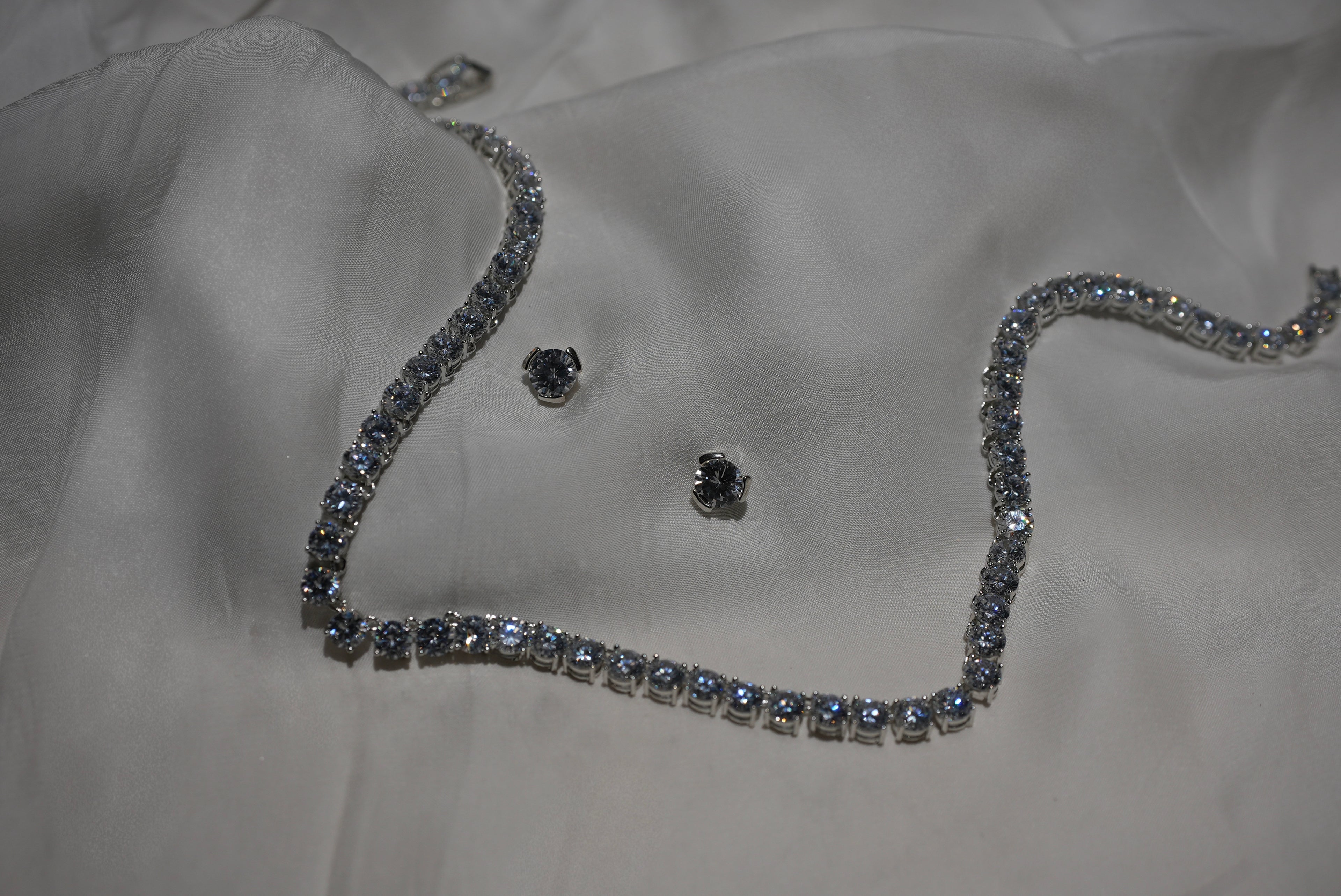 Silver necklace and earrings on a white fabric background